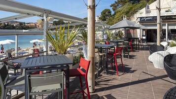 An outdoor patio area with tables and chairs, overlooking a pool and beach.