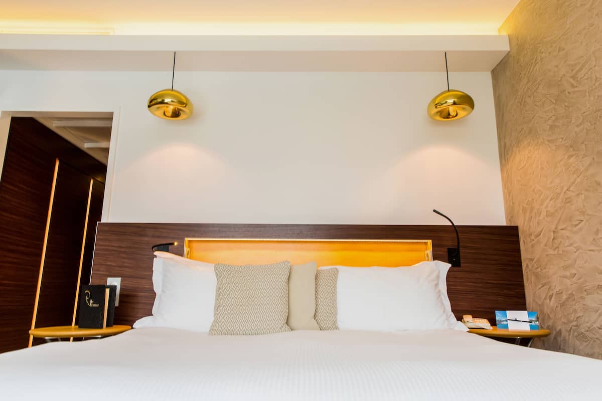 A hotel room with a large bed, two bedside lamps, a wooden headboard, and a nightstand with a phone and a book.