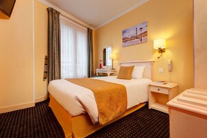 A hotel room with a large bed, a bedside table, a lamp, a painting on the wall, and a carpeted floor.