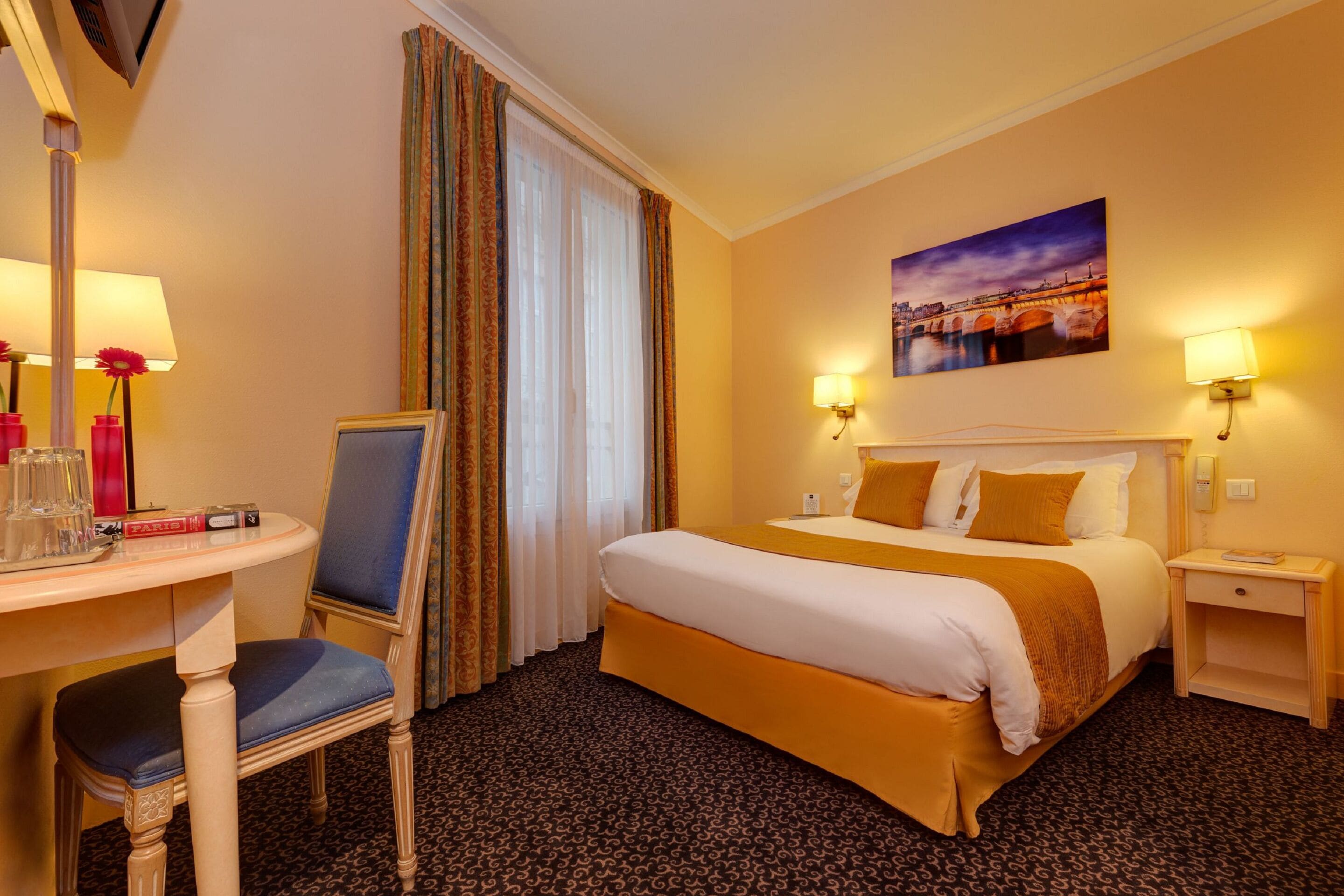 A hotel room with a bed, a desk with a chair, a lamp, a painting on the wall, and a window with curtains.
