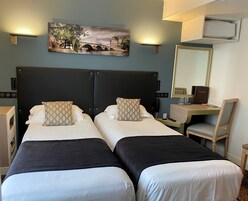 A hotel room with two beds, a desk, a chair, a mirror, and a painting on the wall.