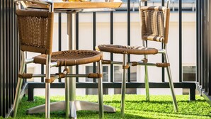 En balkon med et morgenmadsbord, fletstole og udsigt til en bygning med skråtag.