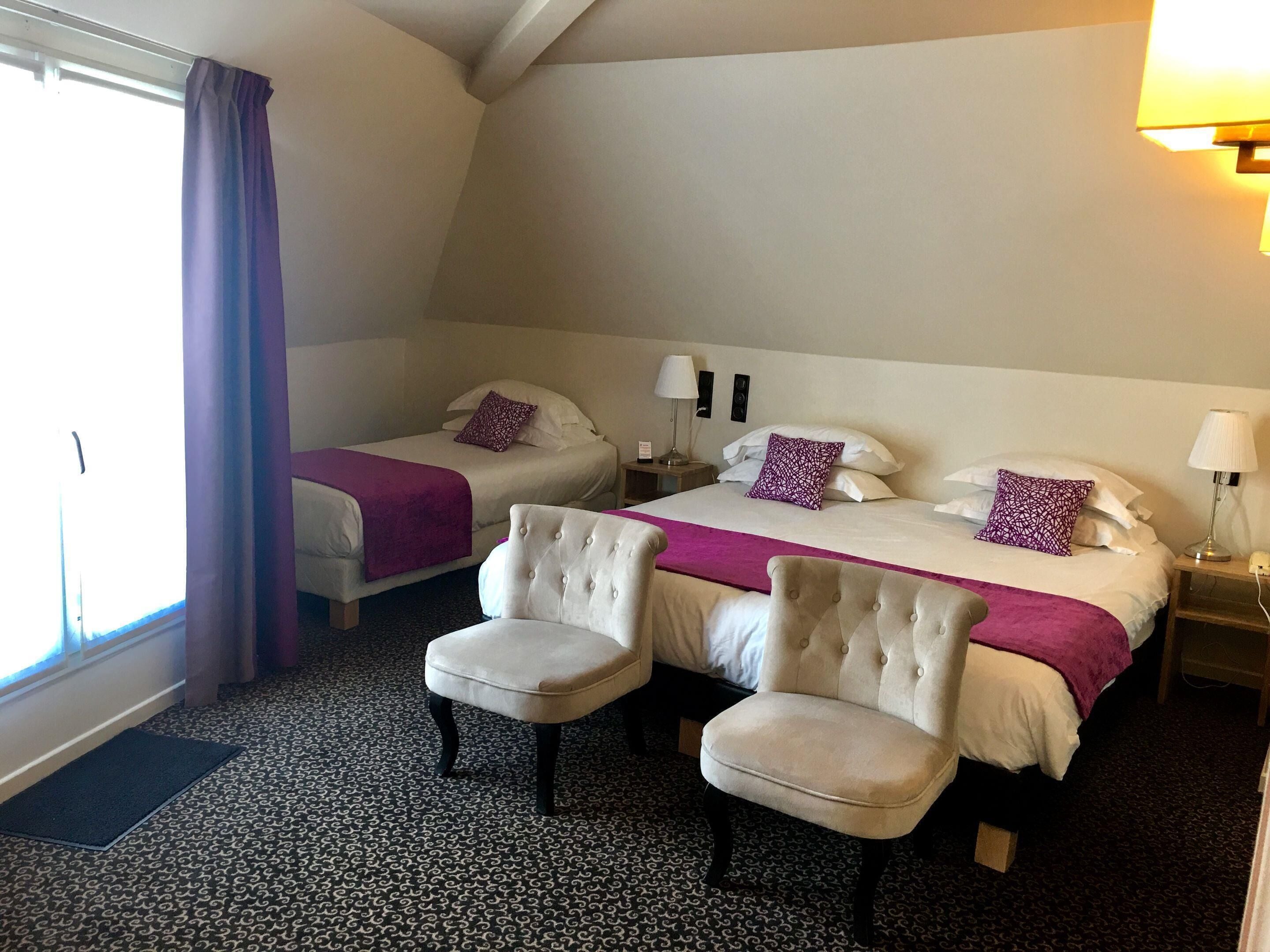 A hotel room with two beds, a sitting area with chairs, a patterned carpet, and a window with curtains.