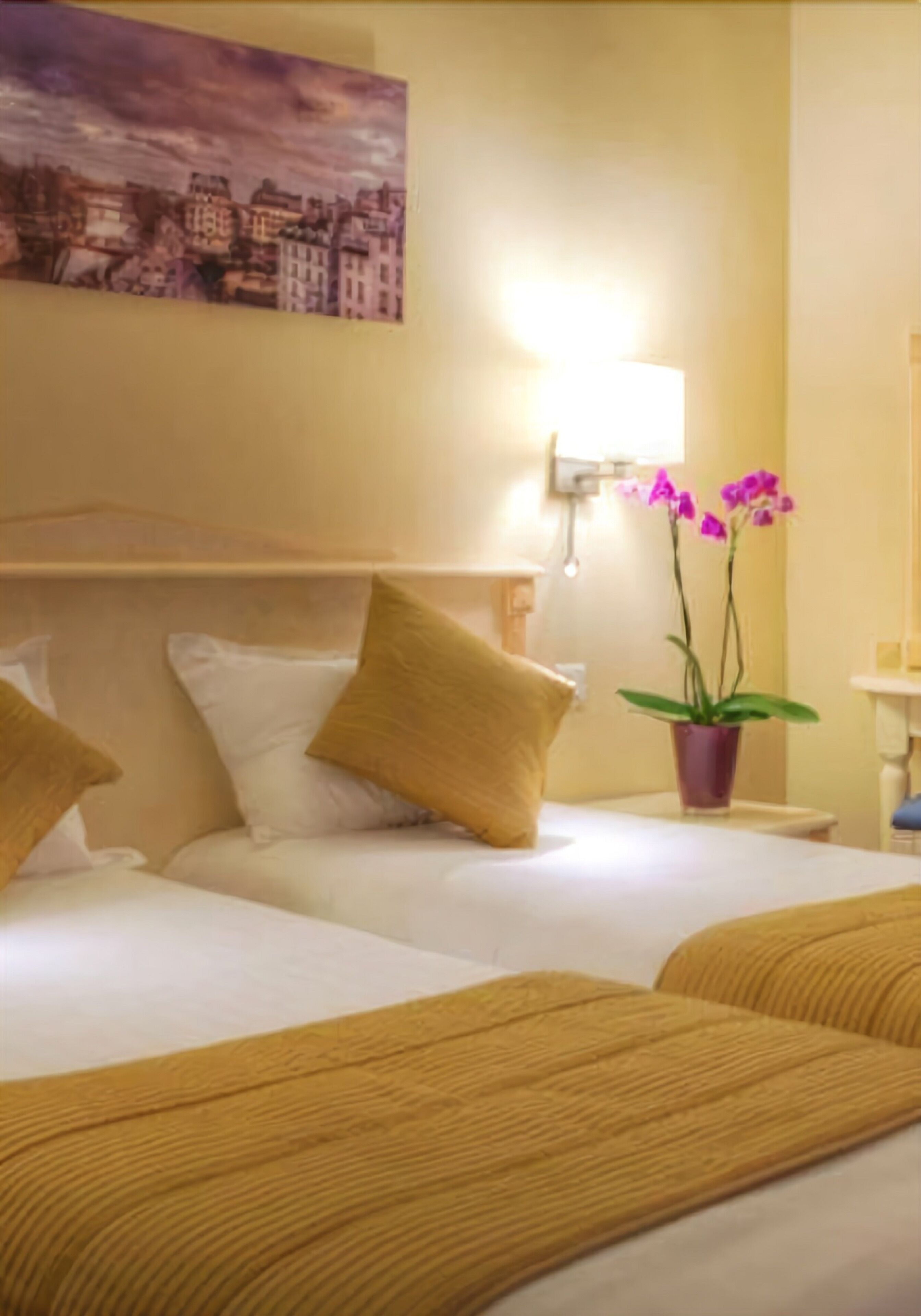 Habitación de hotel con dos camas, un cuadro en la pared, una mesita de noche con una lámpara y una planta en maceta.