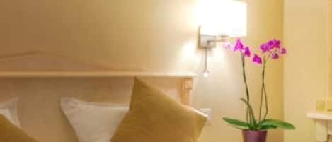 Habitación de hotel con dos camas, un cuadro en la pared, una mesita de noche con una lámpara y una planta en maceta.