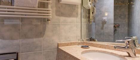 Un baño moderno con pared de azulejos de mármol, un espejo grande, un lavamanos con grifo y un toallero con toallas.
