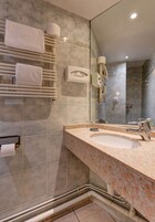A modern bathroom with a marble-tiled wall, a large mirror, a sink with a faucet, and a towel rack with towels.