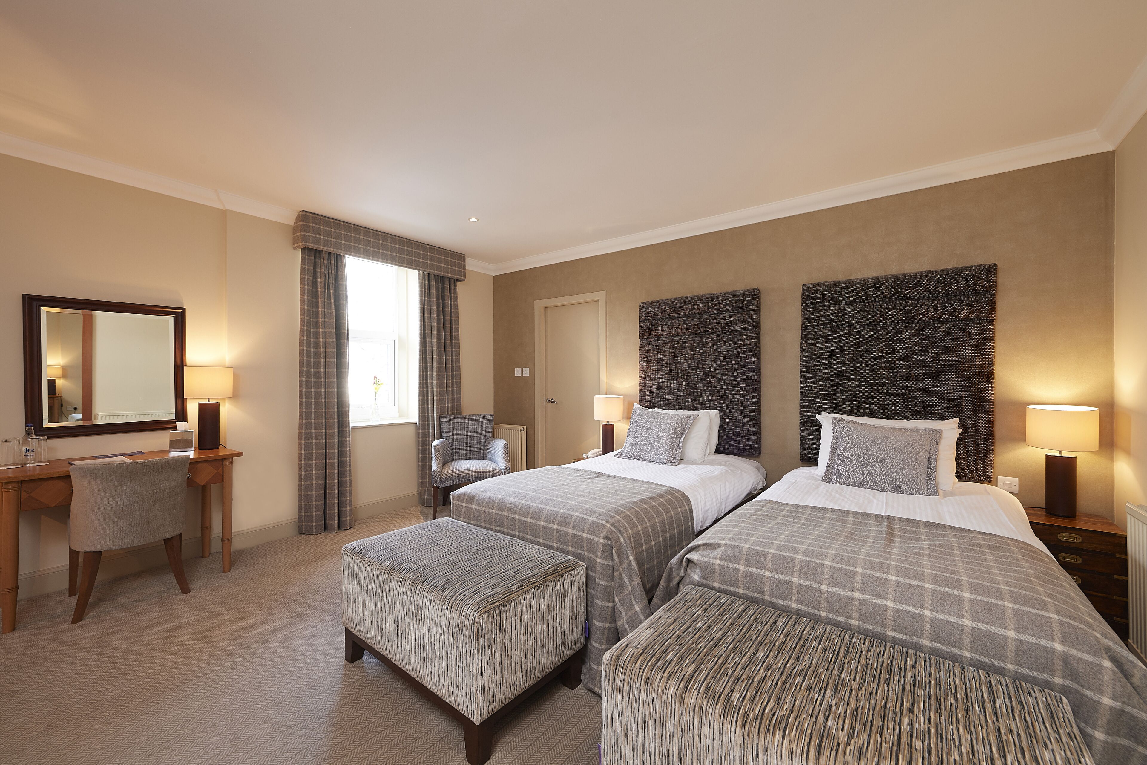 Une chambre d’hôtel avec deux lits, un bureau, une chaise et un grand miroir.