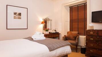 Quarto de hotel com cama, penteadeira, cadeira, escrivaninha, espelho, quadro emoldurado e televisão.