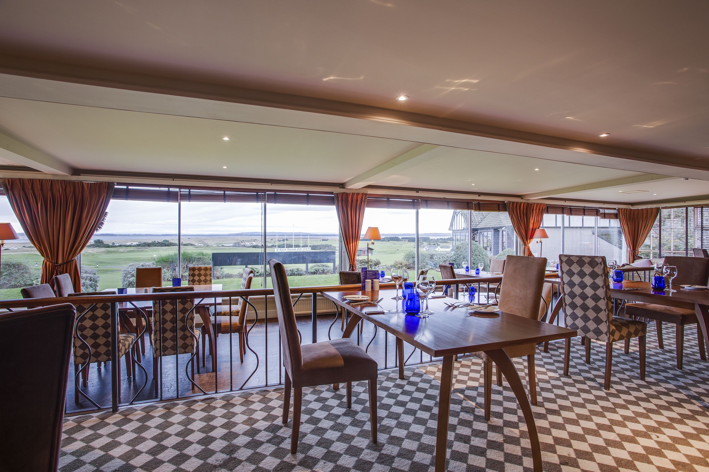 A dining area with checkered flooring, tables, chairs, and large windows offering a view of the outdoors.