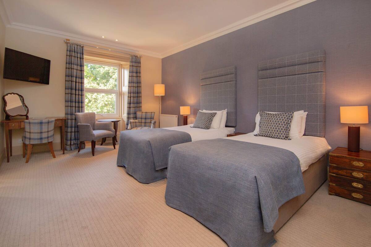A hotel room with two beds, a desk, a chair, and a TV.