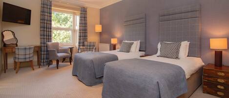 A hotel room with two beds, a desk, a chair, and a TV.