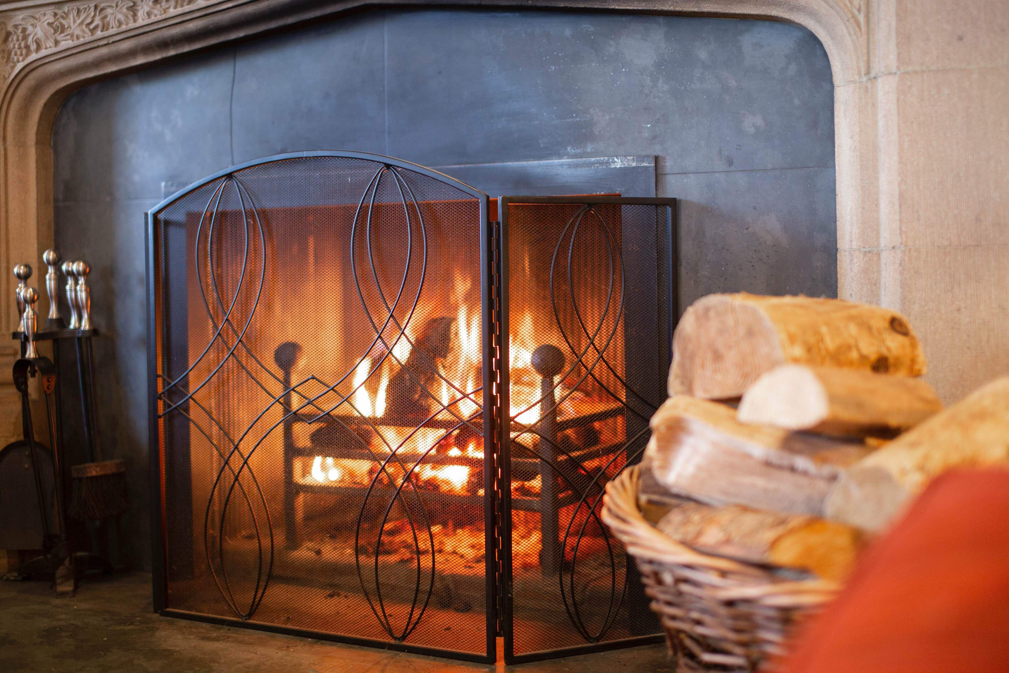 Une cheminée avec un feu, un panier de pain et un paravent en métal.