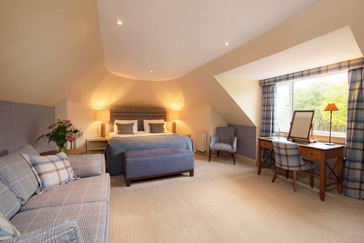 A bedroom with a bed, a desk, a chair, a sofa, and a window with curtains.