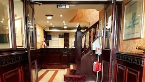 A hotel lobby with a marble floor, a reception desk, a staircase, and a framed picture on the wall. - The Ashley Hotel (Altrincham)