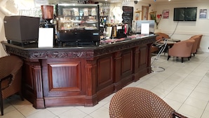 A bar area with a coffee machine, glassware, and a chalkboard menu. There are wicker chairs and a television mounted on the wall. - The Ashley Hotel (Altrincham)
