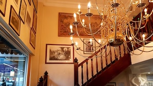 A staircase with a chandelier, framed pictures, and a 'Please mind your head' sign. - The Ashley Hotel (Altrincham)