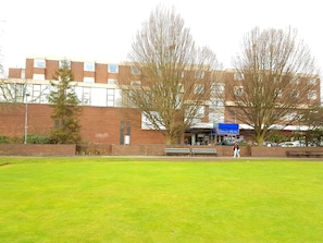 A hotel with a blue sign, a brick building, and a grassy area with benches. - The Ashley Hotel (Altrincham)