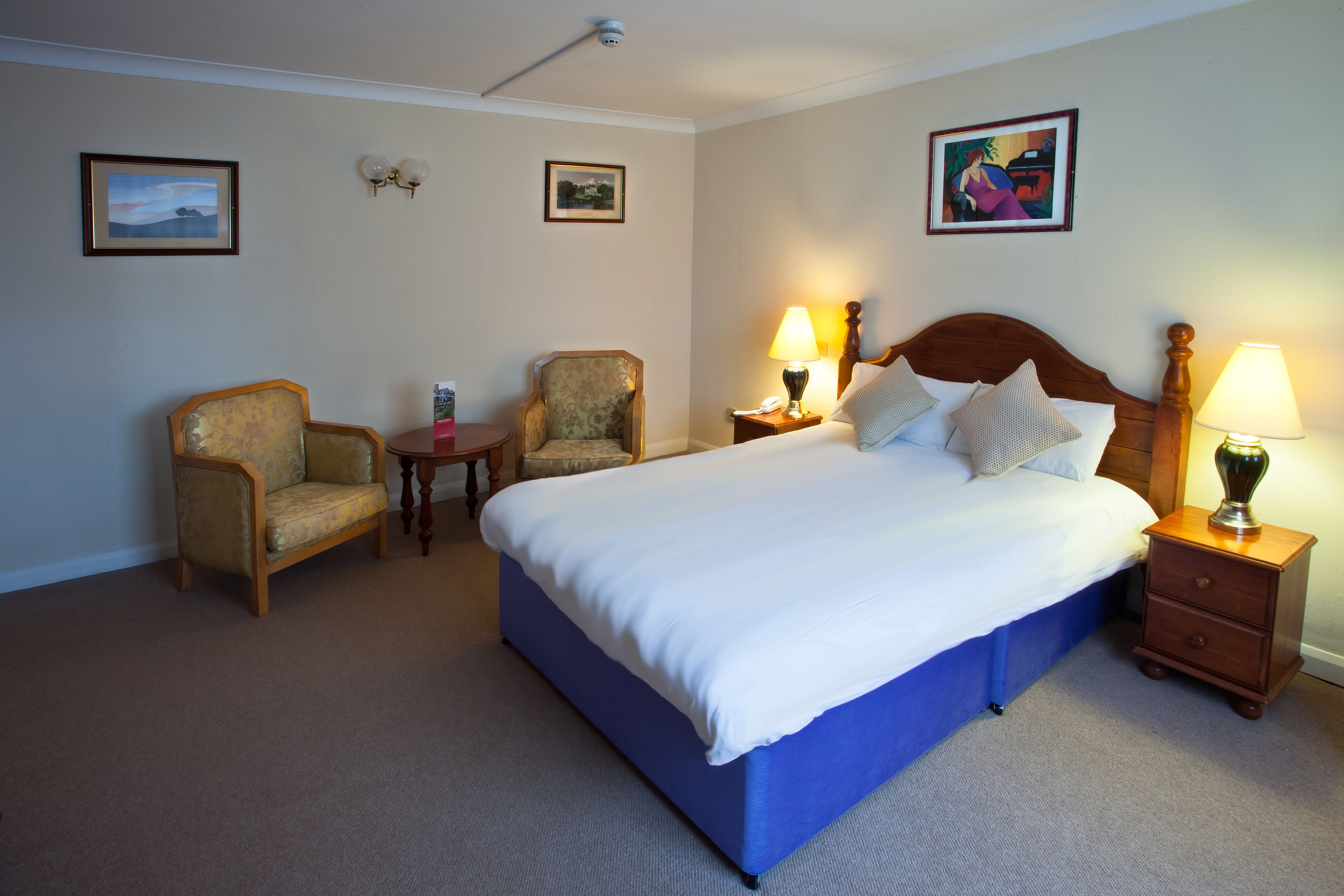 A hotel room with a large bed, two armchairs, a small table, and two bedside lamps.