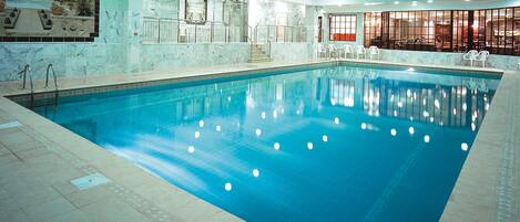 Une piscine intérieure à l’eau claire, avec des murs carrelés et un espace détente équipé de chaises.