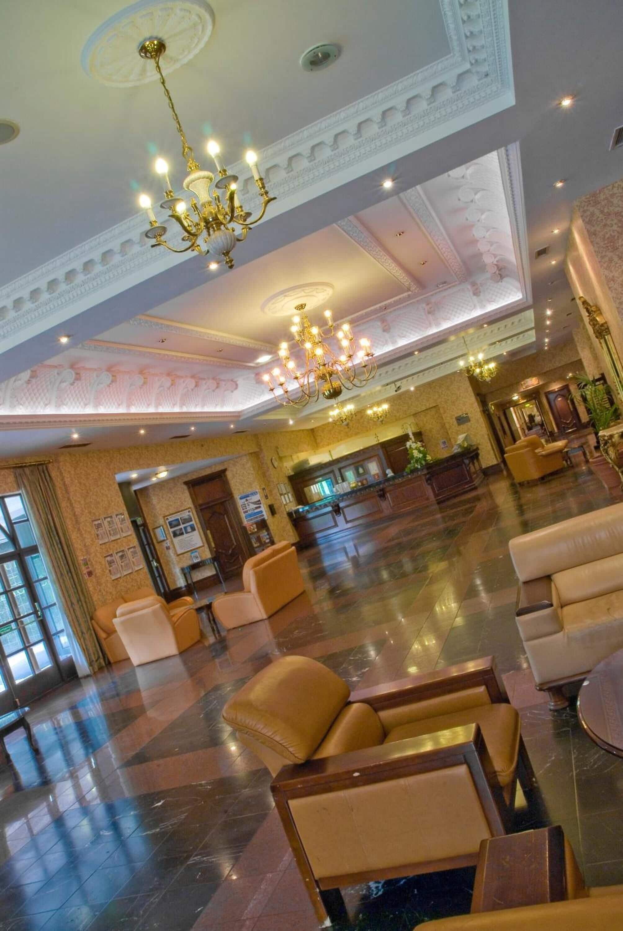 Un vestíbulo amplio con mostrador de recepción, zona de estar y candelabros decorativos.