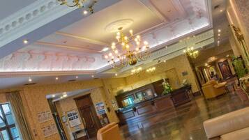 Un vestíbulo amplio con mostrador de recepción, zona de estar y candelabros decorativos.
