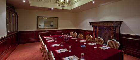 A conference room with a long table, chairs, a chandelier, a mirror, and a fireplace.