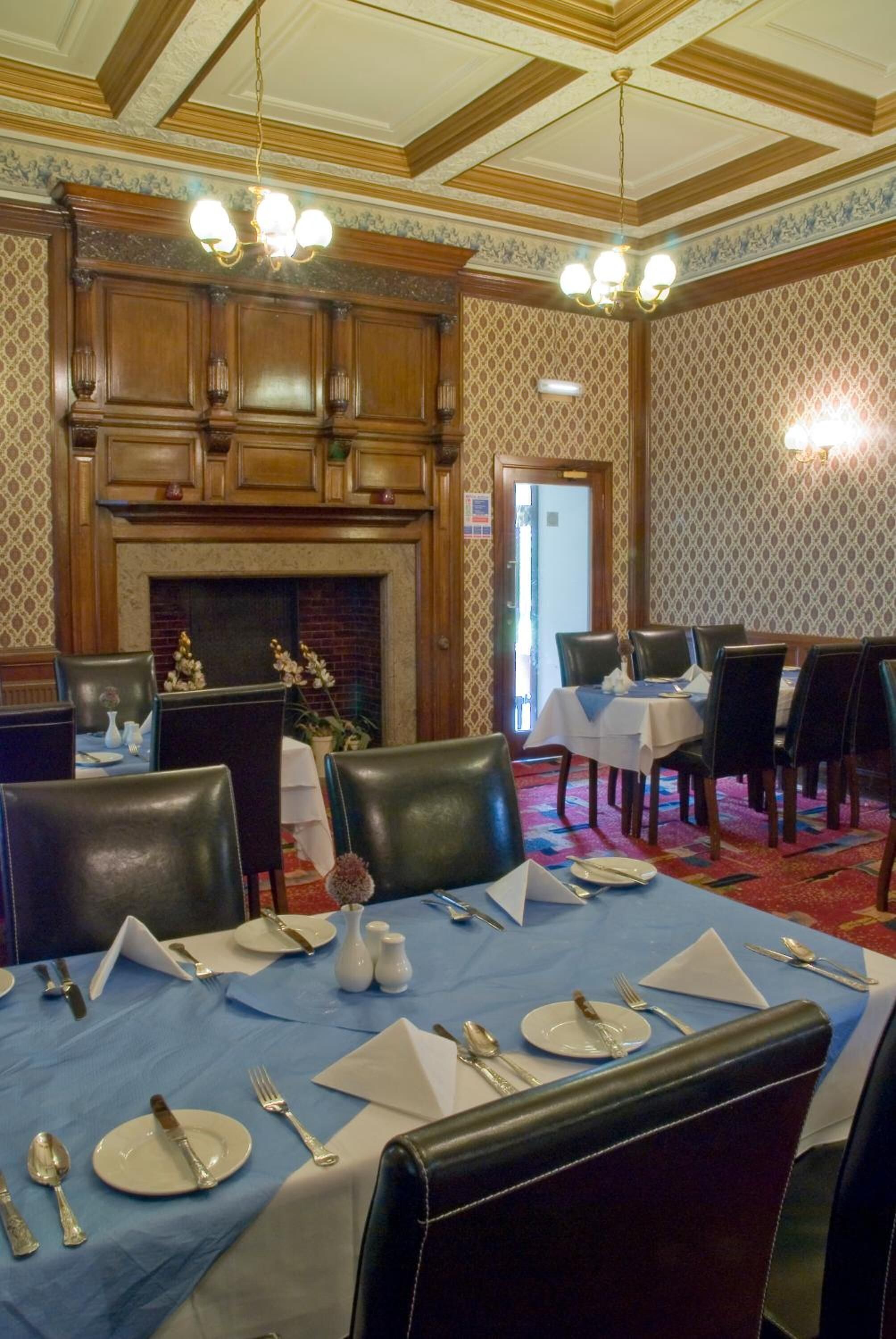 A dining area with tables set for four, wooden paneling, a fireplace, and a chandelier.