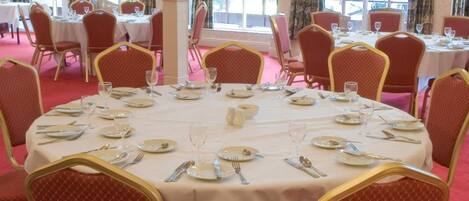 A banquet hall with round tables set for dining, surrounded by red upholstered chairs with gold accents.