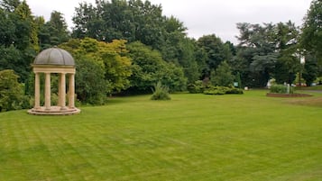 A well-maintained lawn with a classical pavilion and dense trees in the background.