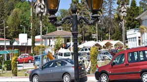 Une scène de rue avec un lampadaire noir, une voiture rouge et une voiture grise garées au bord de la route.