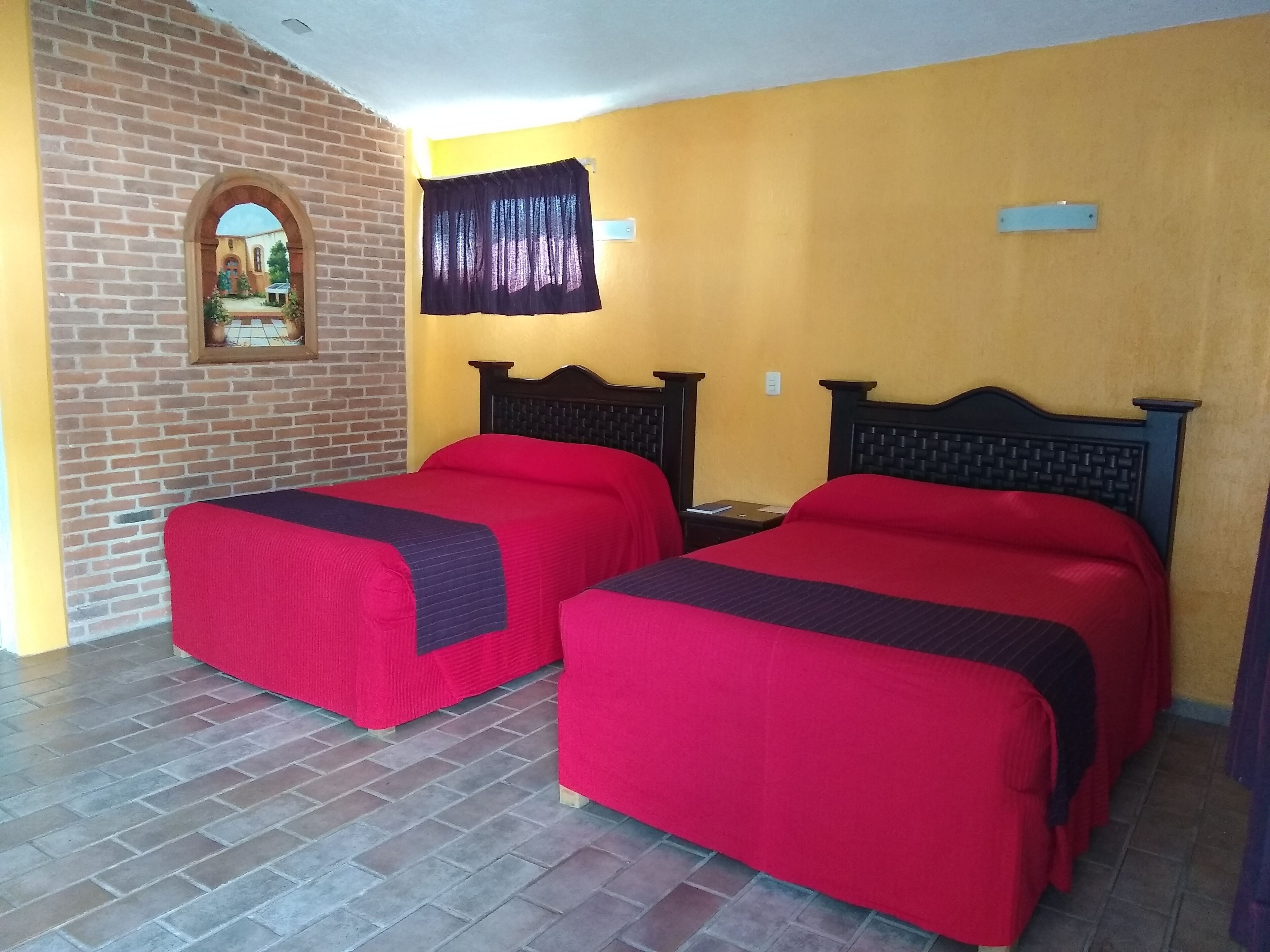 A room with two beds, a brick wall, a yellow wall, and a window with a curtain.