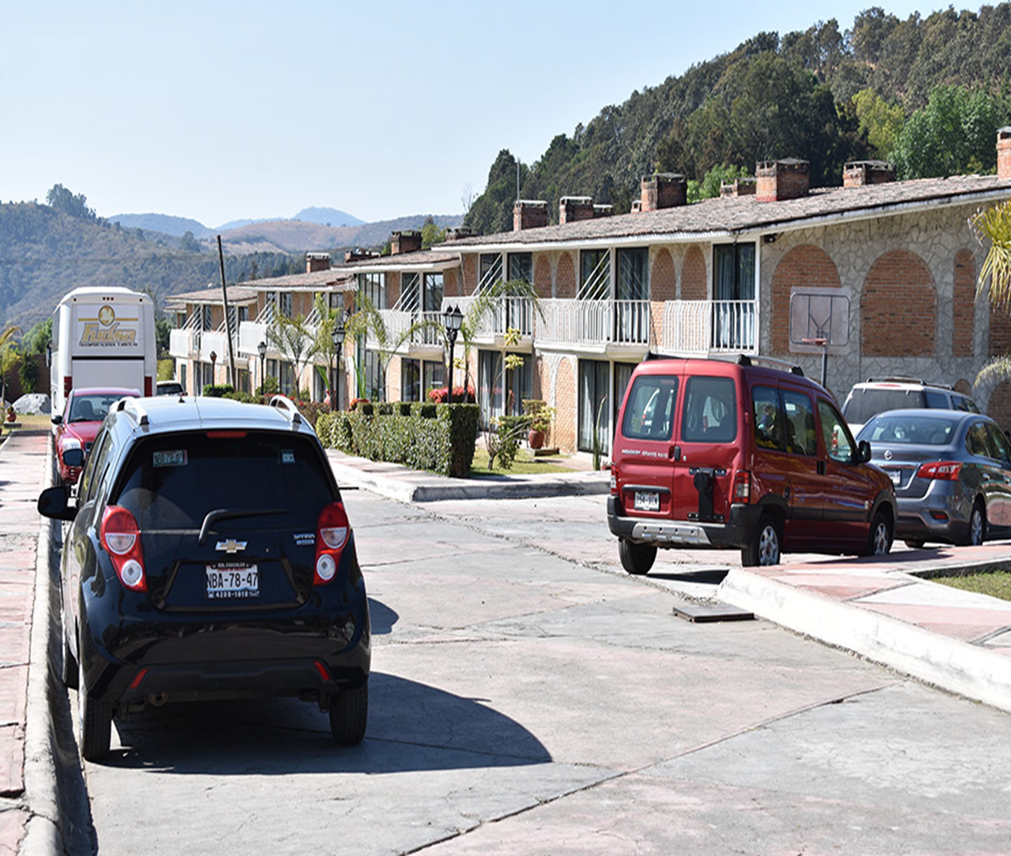 A street view with parked cars, a building with a balcony, and a mountainous background.
