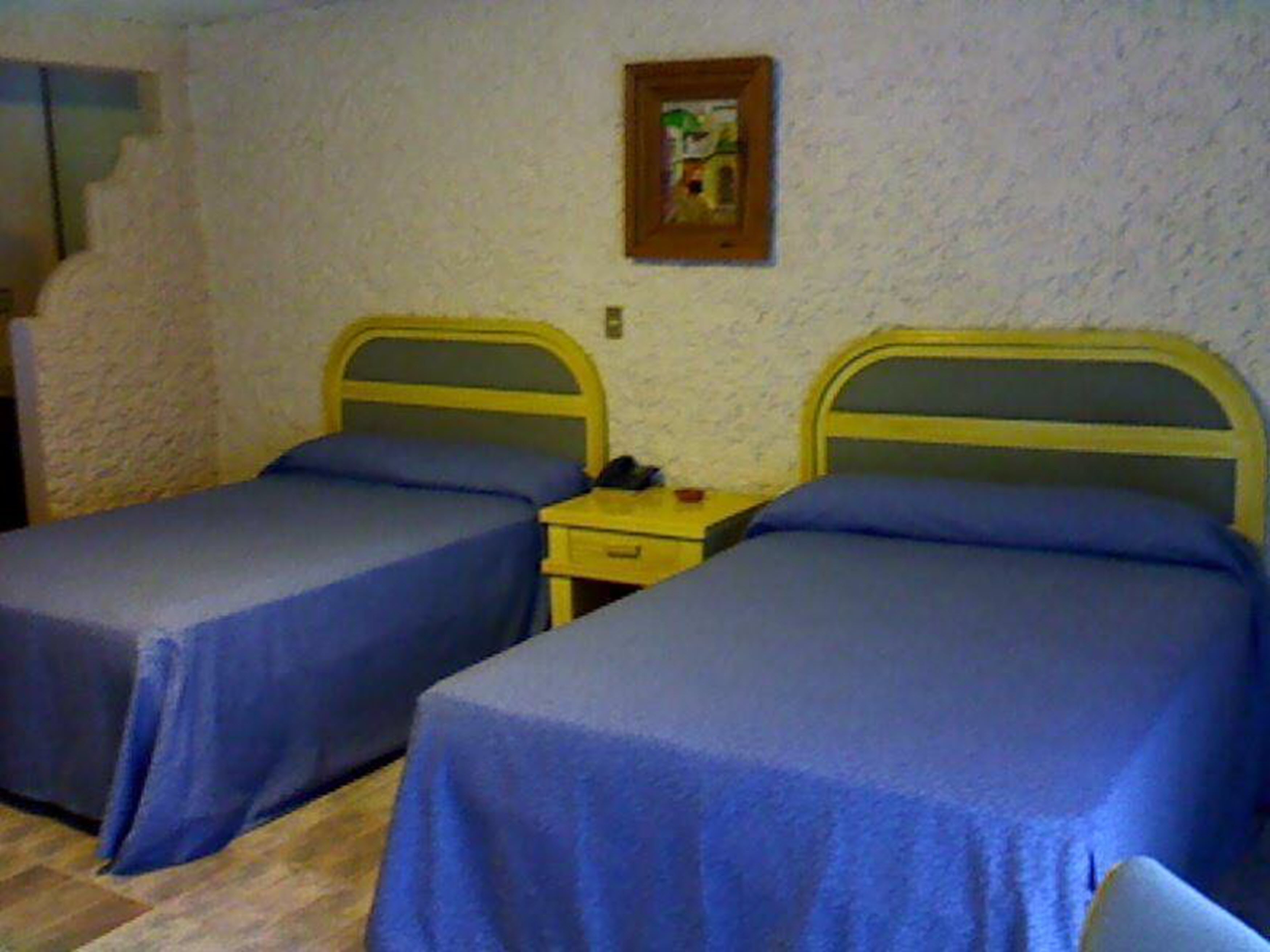 Una habitación con dos camas individuales, una mesita de noche pequeña y un cuadro colgado en la pared.
