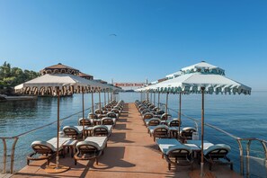 A deck with rows of sun loungers and umbrellas, a sign reading 'Monte-Carlo Beach', and a clear blue sky.