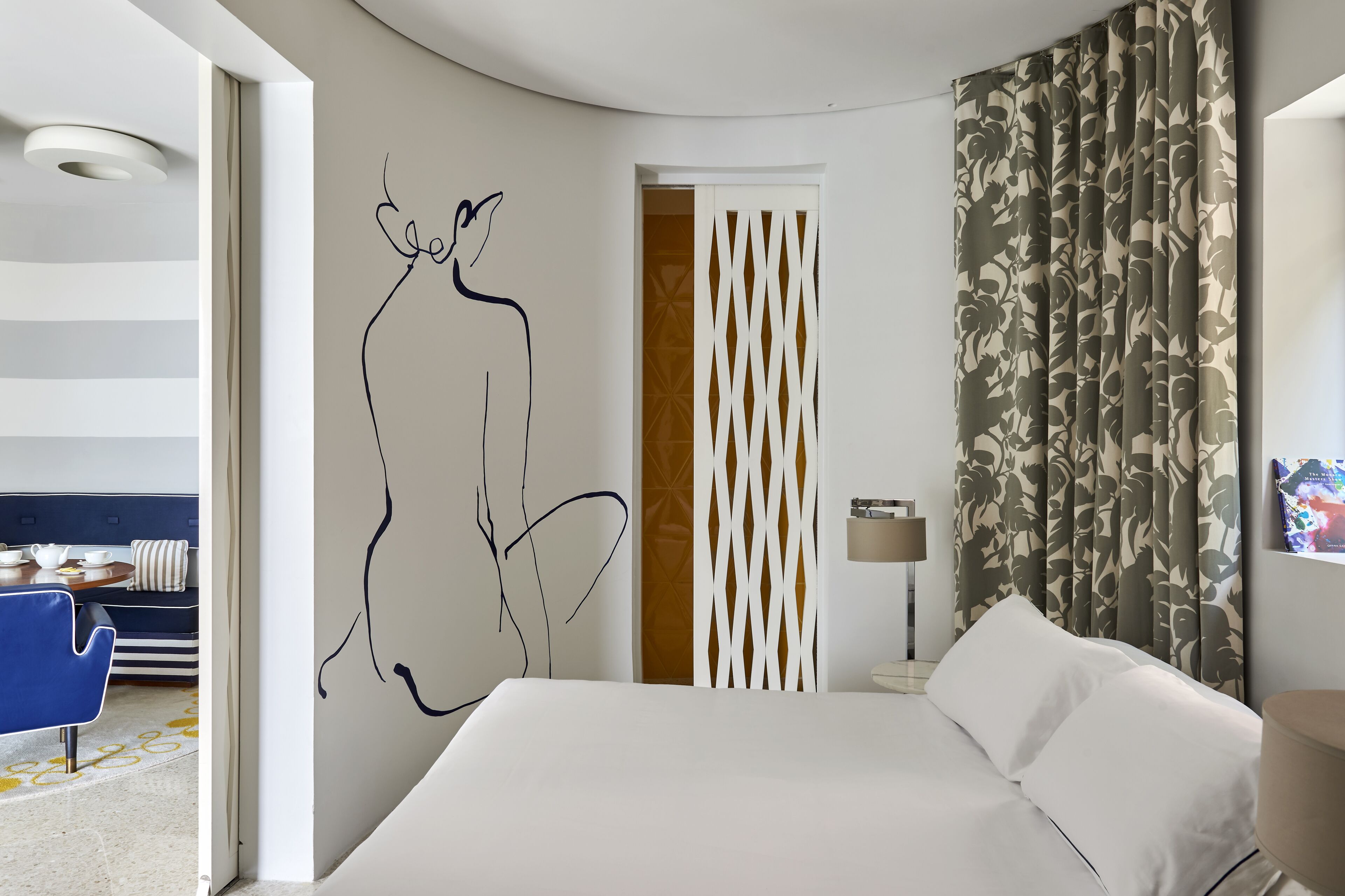 A modern hotel room with a bed, a wall art piece, a patterned curtain, and a decorative partition.
