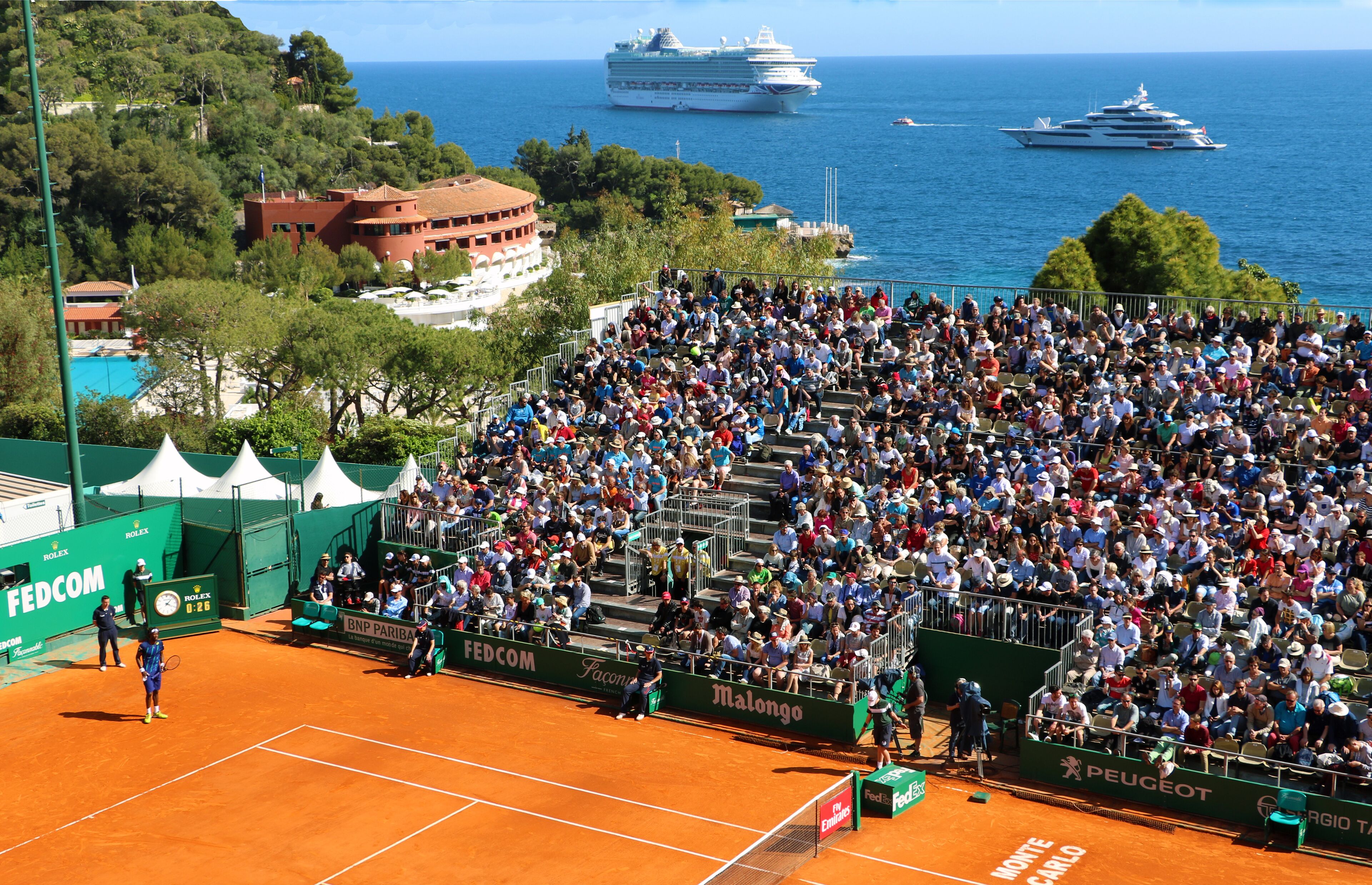 Ein Tennisstadion mit Zuschauern, einem Tennisplatz und Booten im Hintergrund.