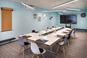 Conference room with a long table, chairs, whiteboard, clock, and projector screen.