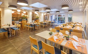 A spacious dining area with multiple tables and chairs, large windows, and ceiling lights.