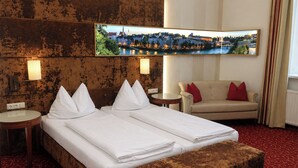 Une chambre d’hôtel avec un lit, un canapé, un banc, un téléviseur fixé au mur et une vue sur le paysage urbain.