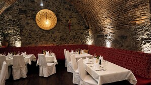 Un restaurant aux murs de pierre, aux tables rondes et aux sièges recouverts d’un tissu rouge à motifs.