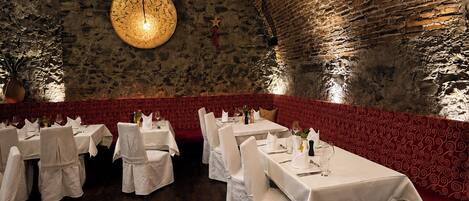 A restaurant with stone walls, round tables, and red patterned upholstery.