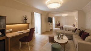 Un salon moderne avec un bureau en bois, un fauteuil rouge, un pouf vert, un canapé beige et un lustre.