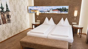 Una cama doble con dos almohadas, una mesita de noche con lámpara, un cuadro de un paisaje urbano y un papel tapiz estampado.