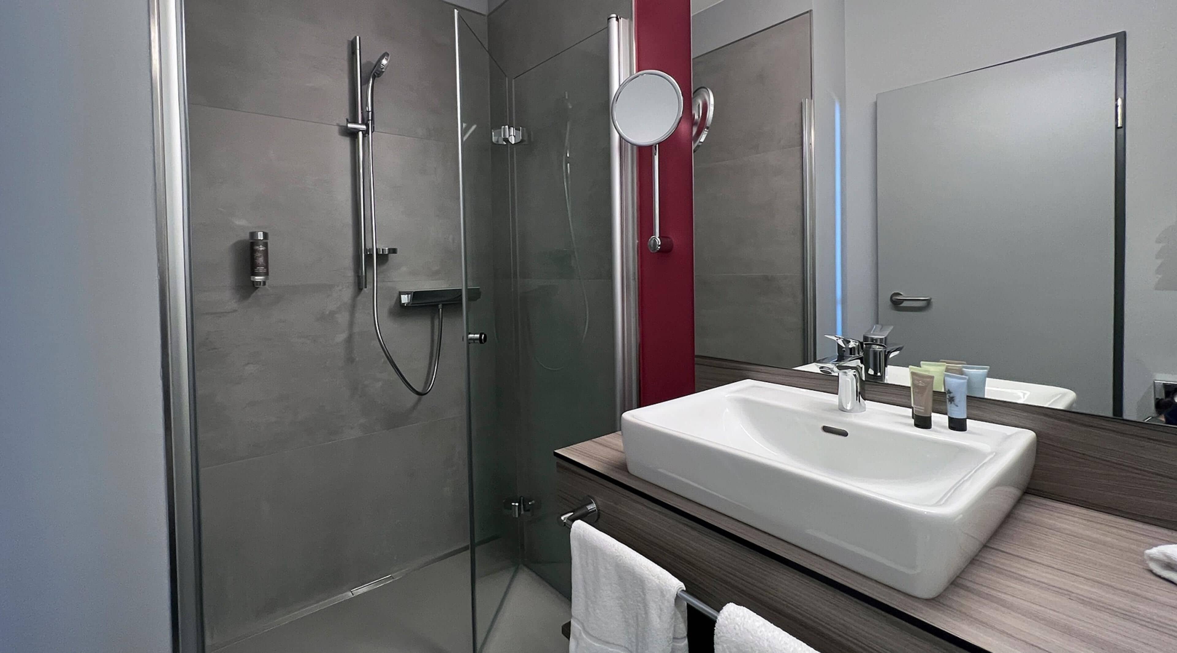 Un baño moderno con ducha de vidrio, lavabo blanco y espejo.