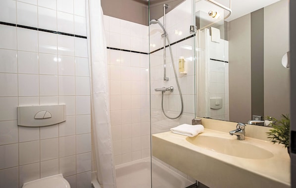 A modern bathroom with a glass shower enclosure, a white toilet, a sink with a mirror, and a towel on the counter. - Median Hotel Lehrte (Lehrte)