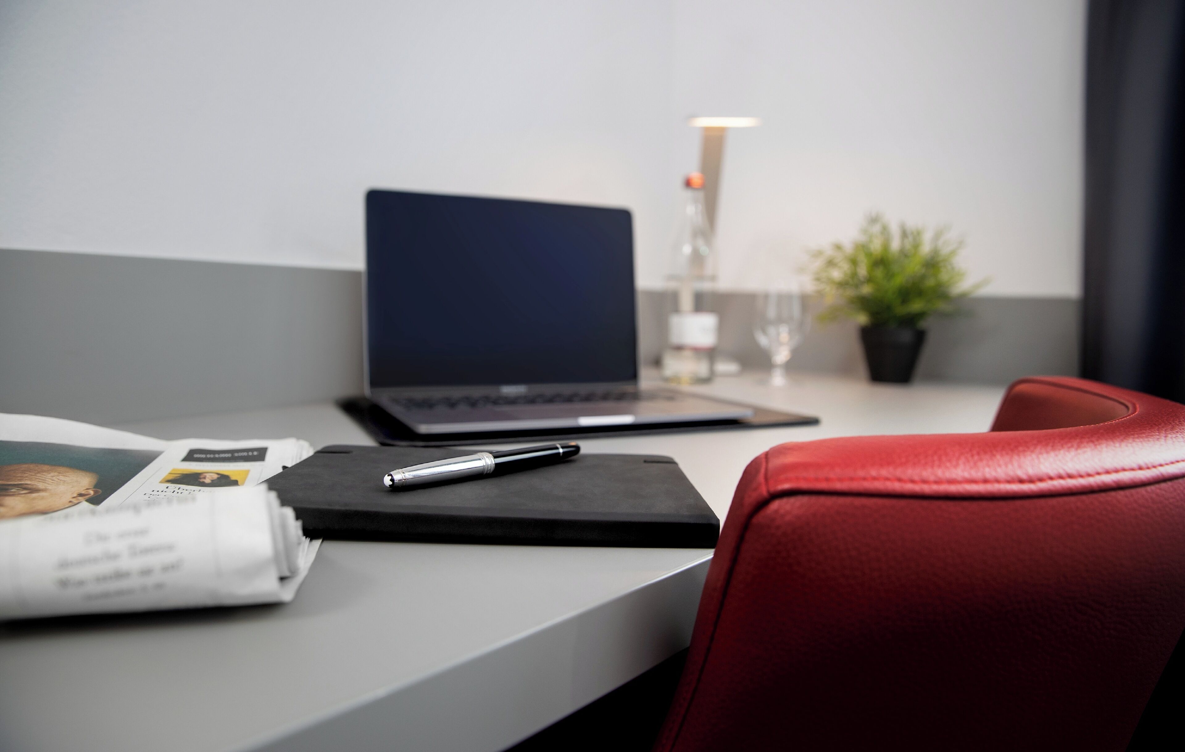 A modern office desk with a laptop, a pen, and a notebook.