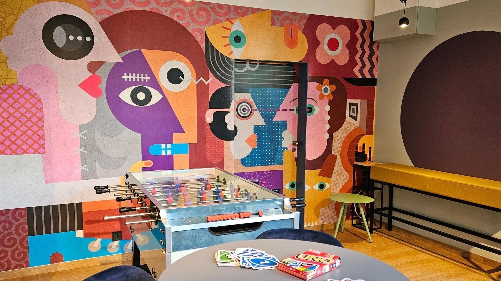 A room with a foosball table, a foosball table in the corner, and a table with cards.