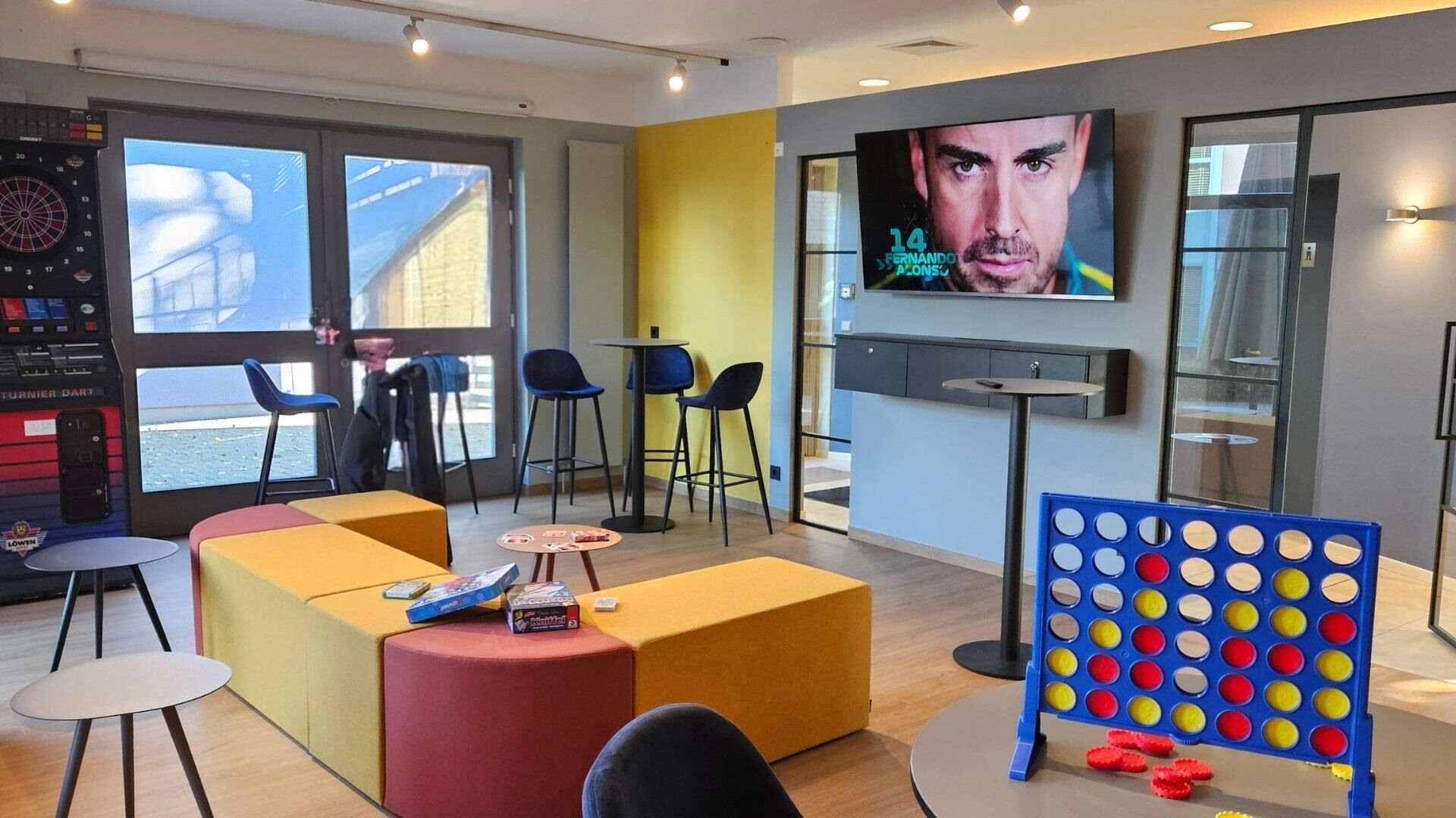Un área de descanso moderna con asientos, un dardo y una pantalla de televisión mostrando una película.