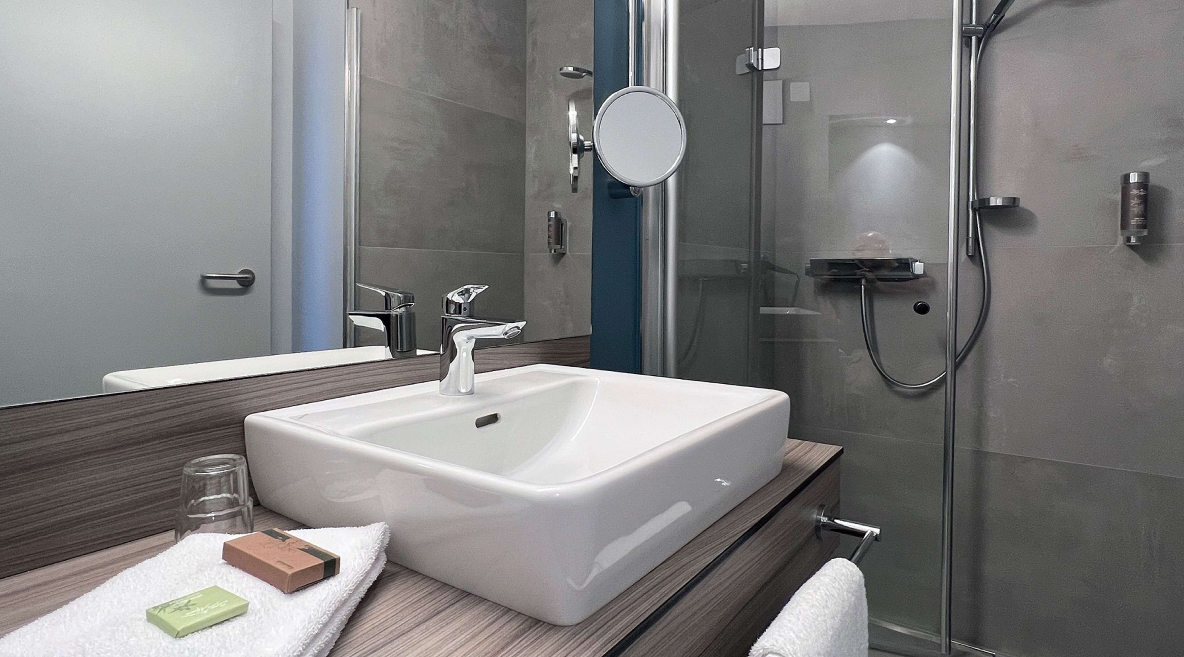 A modern bathroom with a large white sink, a glass shower enclosure, and a mirror above the sink.